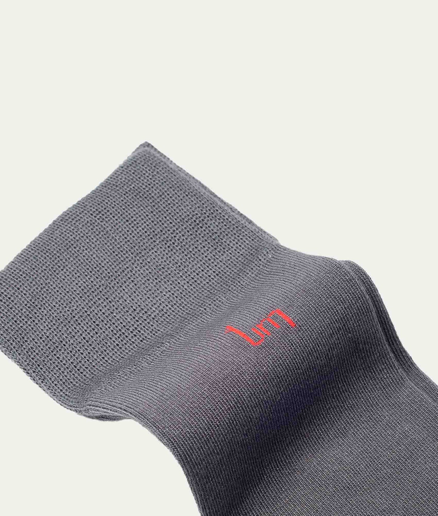 Close-up flatlay lange grijze sok met rood UM (undiemeister) logo