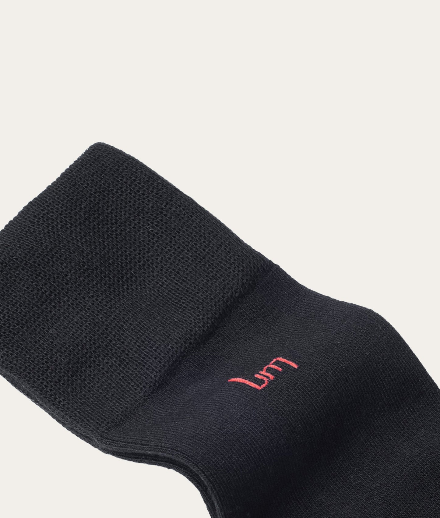 Close-up flatlay lange zwarte sok met rood UM (undiemeister) logo